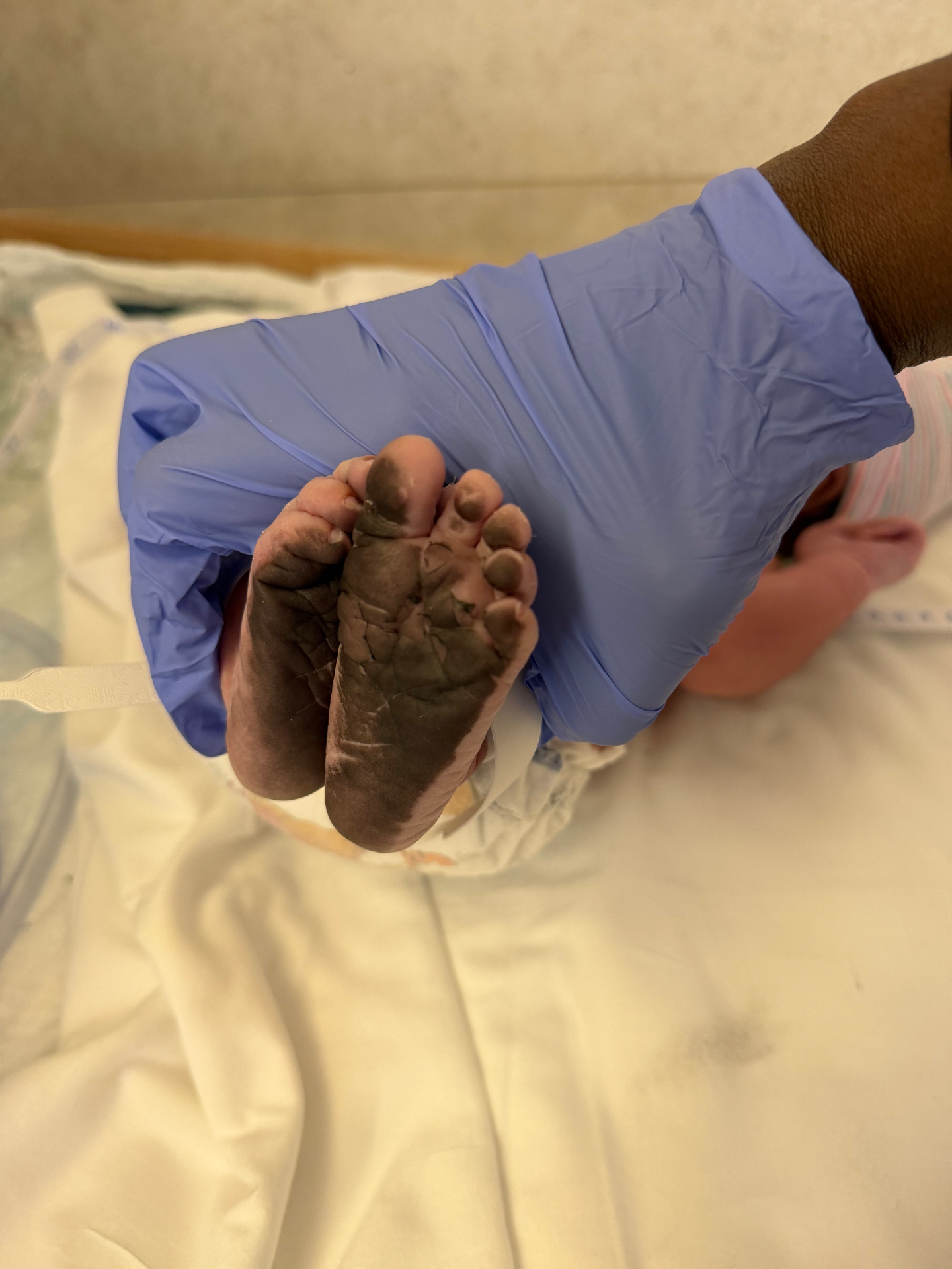A gloved caregiver's hand cradling a newborn's foot